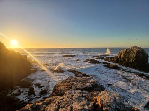 a sunset over the ocean with rocks in the water at Alta Vista de Cahuil in Pichilemu