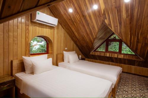 two beds in a room with wooden walls and windows at Hang Mua Ecolodge in Ninh Binh