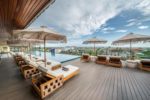 a deck with several beds and umbrellas and a pool at TUI BLUE Berawa Hotel and Villas in Canggu