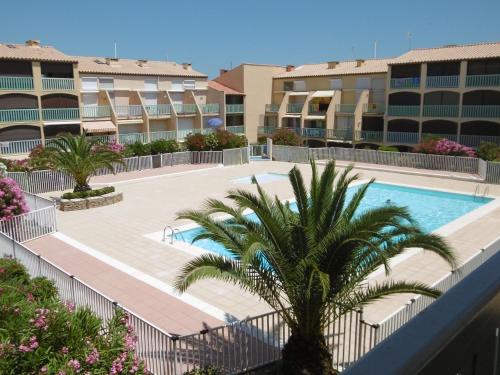 - une piscine avec un palmier et des bâtiments dans l'établissement T2 RDC avec Terrasse, Piscine & Parking - Proche Vieux Village de Gruissan - FR-1-796-20, à Gruissan