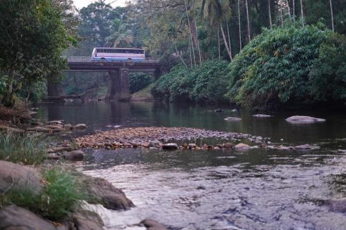 a bus driving on a bridge over a river at Athirapilly Ontherocks in Athirappilly