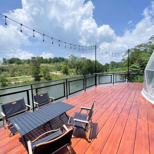 a deck with a picnic table and chairs on the water at River Hill Khaokho in Khao Kho