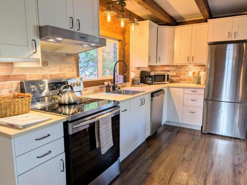 a kitchen with white cabinets and stainless steel appliances at 4 Mile Creek Cabin (Creekside) in Nelson