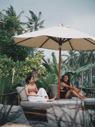 two women sitting on beds under an umbrella at Desa Cabins in Balian