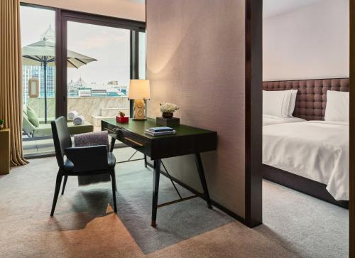 a hotel room with a desk and a bed and a window at Rosewood Bangkok in Bangkok