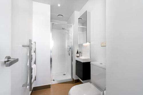 a white bathroom with a toilet and a shower at The Heart of City Living with Incredible City & Skytower View Nearby Queen St in Auckland
