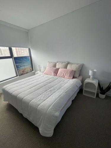 a white bedroom with a large bed with pink sheets at 1 Bedroom Apartment with balcony in Sydney