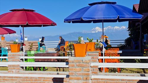 two umbrellas and tables and chairs with people in the background at Hotel Mystic Kakani in Kakani