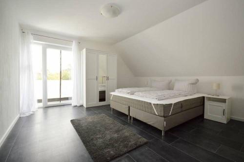 a white bedroom with a bed and a large window at Ferienhaus-Ankerplatz in Norden