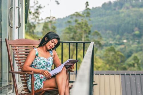 a woman sitting on a chair reading a magazine at Wild Flower Waterfall Villa in Talawakele