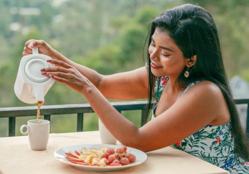 a woman pouring coffee on a table with a plate of food at Wild Flower Waterfall Villa in Talawakele