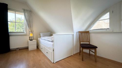 a white bedroom with a bed and a chair at Reetdachhaus - Reet am See in Börgerende-Rethwisch