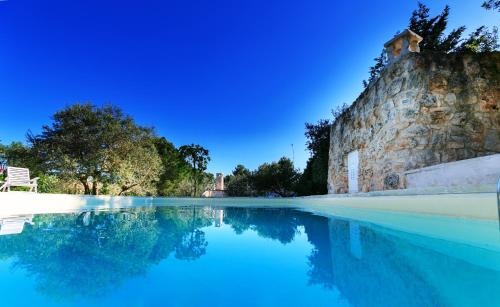 a swimming pool with blue water and a stone wall at Le Dimore di Trulli Mandorlo con piscina esclusiva in Putignano