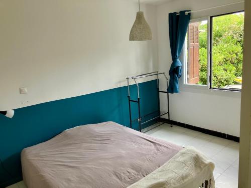 Cet appartement comprend une chambre dotée d'un lit avec un mur bleu et une fenêtre. dans l'établissement Maison bord de mer, à Hyères