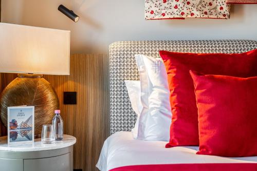 a bed with red and white pillows and a lamp at Maison Boissière BARNES Residences in Paris