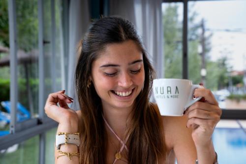 a woman is smiling while holding a coffee cup at NURA Boreal in Playa de Palma