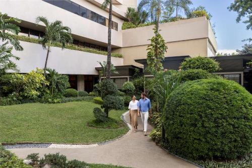 a man and woman walking down a path in front of a building at Dusit Thani Manila in Manila