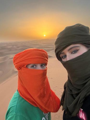 two women standing on the beach with the sunset in the background at Touareg Desert Camp Erg Chigaga in El Gouera