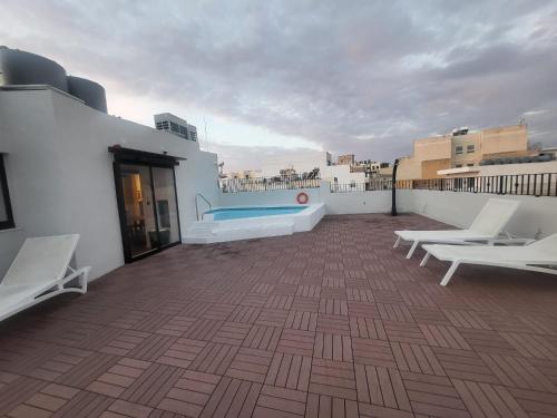 a rooftop with a swimming pool and two white chairs at Carlton Hotel in Sliema
