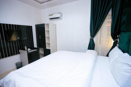 a bedroom with a white bed and a window at Cupid's Corner Luxury Hotel and Apartments in Benin City
