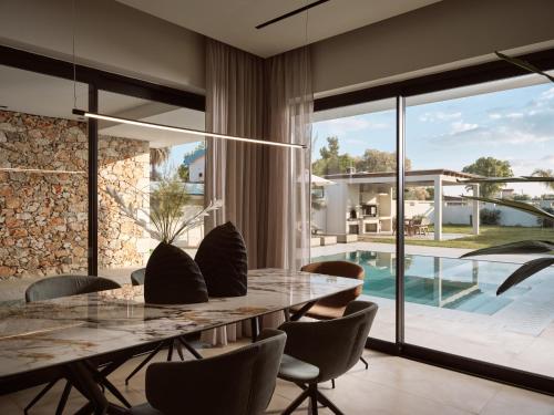 a dining room with a table and chairs and a swimming pool at Vorto Luxury Villas, a Signature Island Retreat, By ThinkVilla in Zakynthos