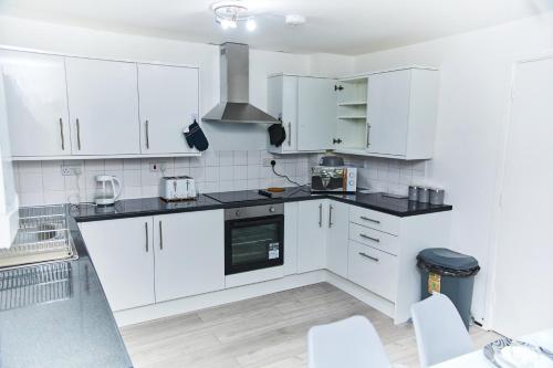 a kitchen with white cabinets and black counter tops at Emerald Haven 5 Star Proximity in London