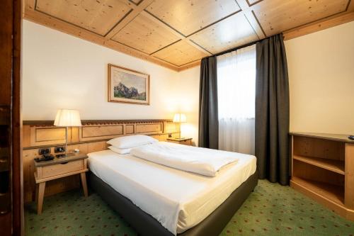 a hotel room with a large bed and a window at Croce Bianca Leisure & Spa Hotel in Canazei