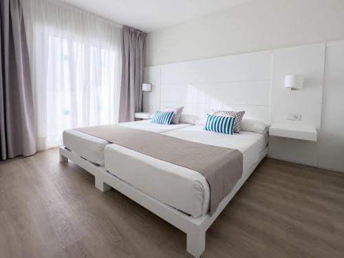 a white bedroom with a large bed with blue pillows at BLUESEA Club Martha's in Cala d´Or