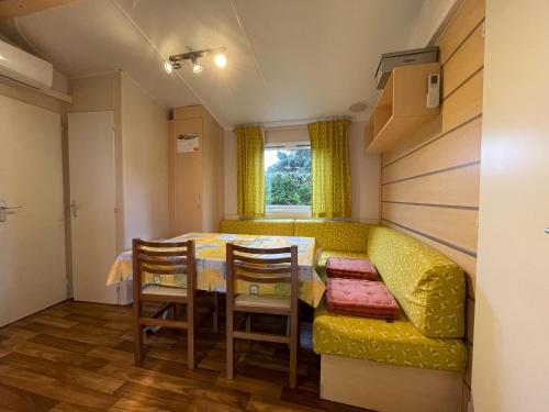 une salle à manger avec une table et un canapé jaune dans l'établissement Bungalow N52 - 6 personnes au calme - Camping Le Ried Boofzheim, à Boofzheim