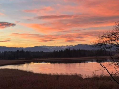 a sunset over a lake with mountains in the background at Gartensee Chalet in Seeshaupt in Seeshaupt