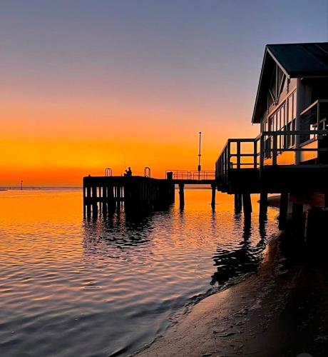 a sunset over the water with a pier and a house at Yellow Door Villa in Barwon Heads