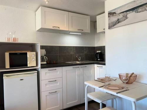 une cuisine avec des armoires blanches et une table avec un micro-ondes dans l'établissement Résidence Port Nature Colline 6 - Studio 2 pers- Port Nature Col 6 MAE-6224, au Cap d'Agde