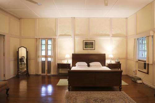 a bedroom with a bed and two tables and a mirror at Chowkidinghee Heritage Tea Bungalow in Dibrugarh