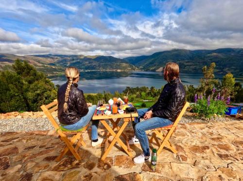 two people sitting at a table with a view of a lake at Pacucha Glamping in Andahuaylas