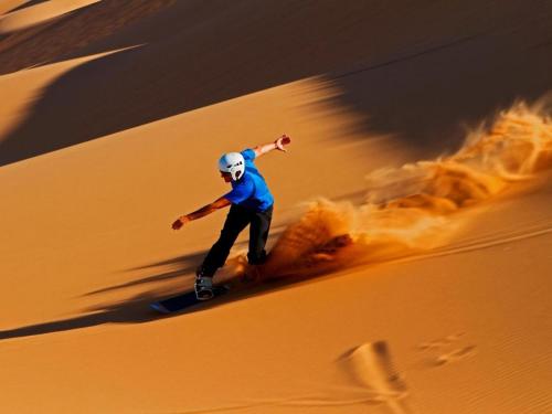 a man riding a snowboard in the desert at Erg Merzouga Desert Camp in Merzouga