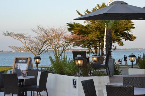 a patio with tables and chairs and an umbrella at Hotel et Spa Les Cleunes Oléron in Saint-Trojan-les-Bains