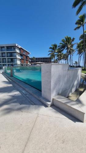a swimming pool with palm trees and a building at Flat Recanto Muro Alto - Porto de Galinhas in Ipojuca