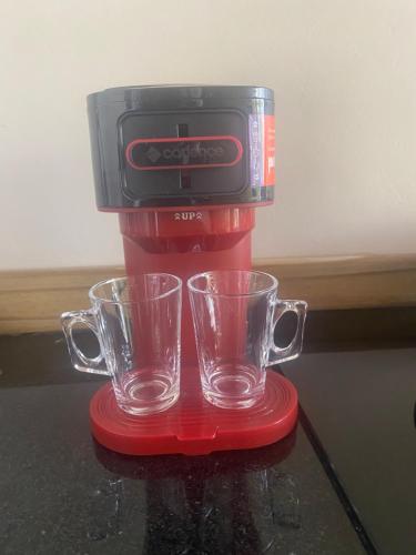 a red coffee maker with two glasses on a table at Loft Chalé Recanto da Natureza in Imbituba