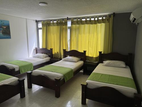 three beds in a room with yellow curtains at Hotel Inambu Villavicencio in Villavicencio