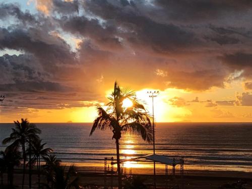 a sunset on the beach with a palm tree at Apartamento Peruibe pé na areia!!! in Peruíbe