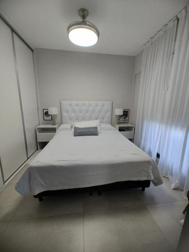 a white bedroom with a large bed and a large window at Departamento Margui in San Pedro
