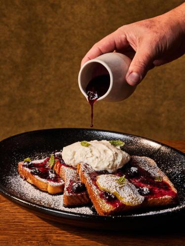 a person drizzling syrup on a plate with french toast at Asher Adams, Autograph Collection in Salt Lake City