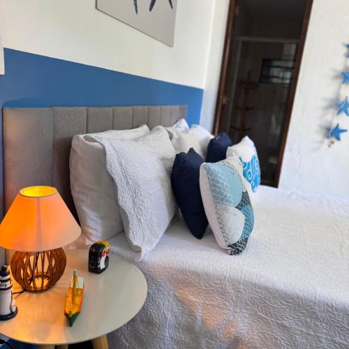 a bed with white pillows and a table with a lamp at POUSO DE ICARO - POUSADA NO CENTRO de PARATY in Paraty