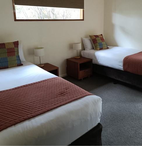 a room with two beds and two tables with lamps at Stewarts Bay Lodge in Port Arthur