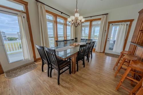 a dining room with a table and chairs and windows at Frolic Inn OBX - Semi Soundfront Retreat, Pool, Hot Tub, Boat Ramp, Elevator, Media & Game Room in Rodanthe