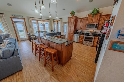 a kitchen with wooden cabinets and a kitchen island with bar stools at Frolic Inn OBX - Semi Soundfront Retreat, Pool, Hot Tub, Boat Ramp, Elevator, Media & Game Room in Rodanthe