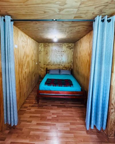 a bed in a wooden room with blue curtains at Cabañas Amanecer Sector Campo 1 in Castro