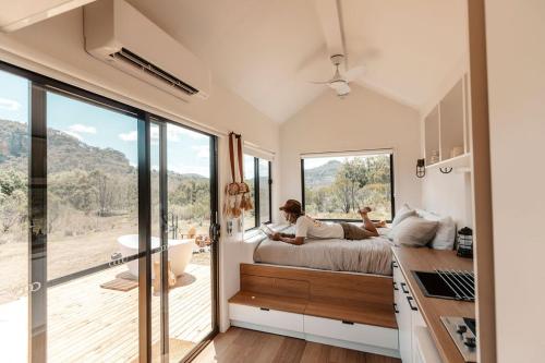 a woman laying on a bed in a room with a large window at Tiny Aura in Rylstone