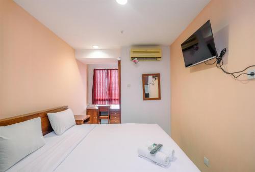 a bedroom with a white bed with a tv on the wall at Classic and Cozy Studio at Cinere Bellevue Suites Apartment By Travelio in Depok