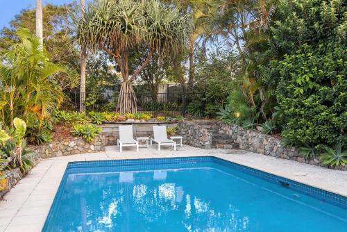 a swimming pool in a yard with two chairs and trees at Pool side Luxury pet friendly - walk to the beach in Alexandra Headland